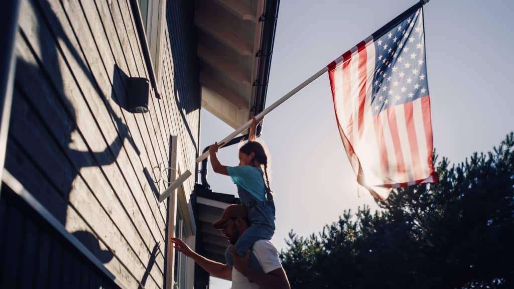 Father with daughter on shoulders hoisting up flag