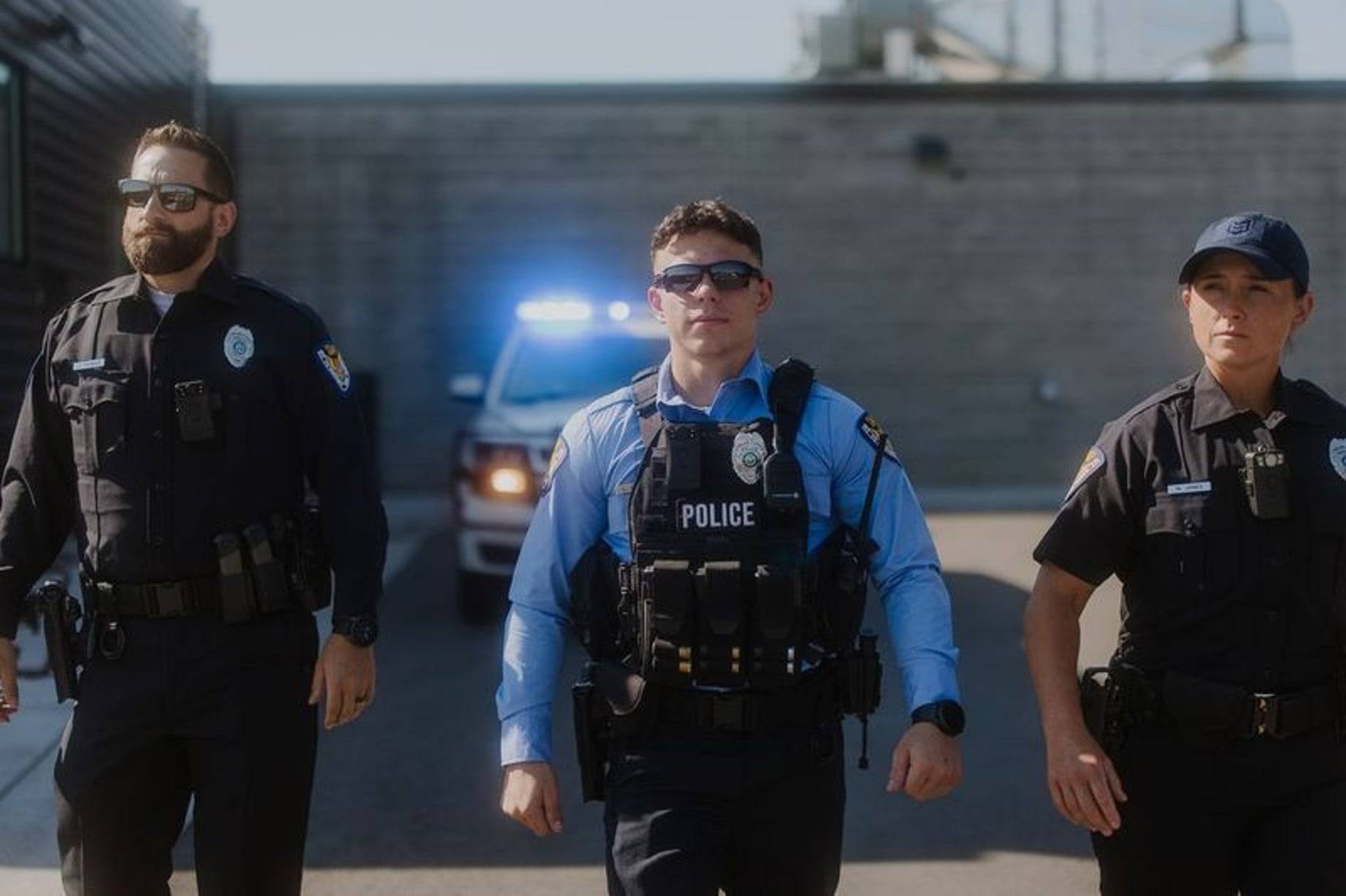Police officers walking in front of car with siren lights on